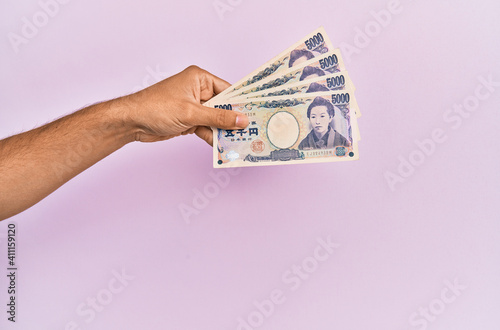 Hispanic hand holding 5000 japanese yen banknotes over isolated pink background.