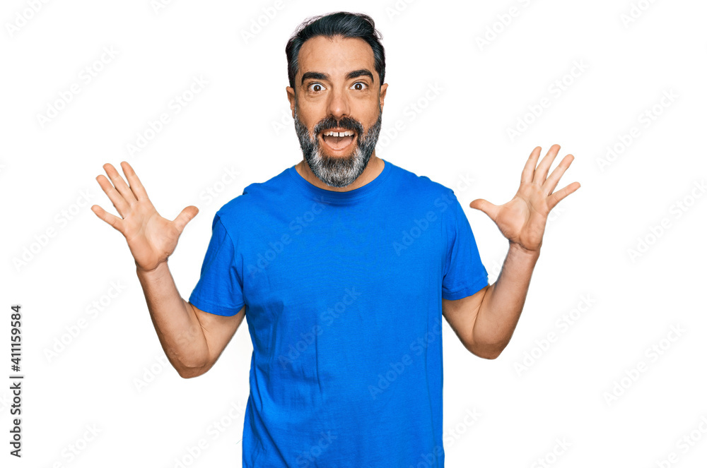 Fototapeta premium Middle aged man with beard wearing casual blue t shirt celebrating crazy and amazed for success with arms raised and open eyes screaming excited. winner concept