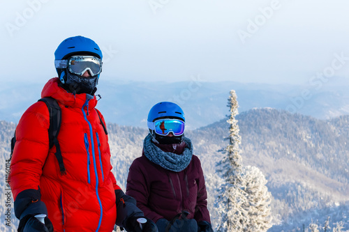 A couple of skiers boy and girl are looking at the camera on the background of the mountains. Frosty winter day