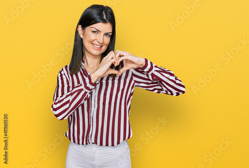 Beautiful brunette woman wearing striped shirt smiling in love doing heart symbol shape with hands. romantic concept. © Krakenimages.com
