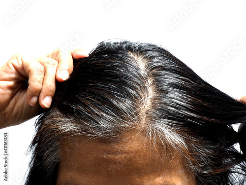 A woman shows her grey hair roots, standing in front of white background. She's pulling her hair with her hands.
People, beauty concept.