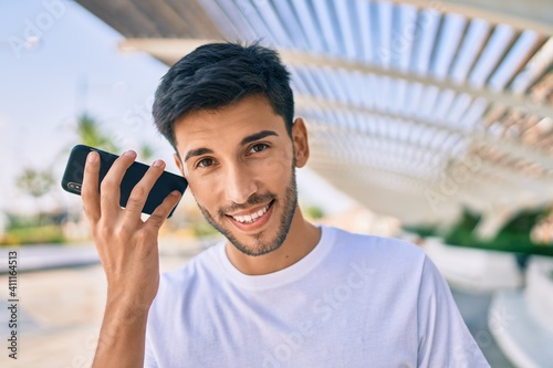 Young latin man smiling happy listening audio message using smartphone at the city.