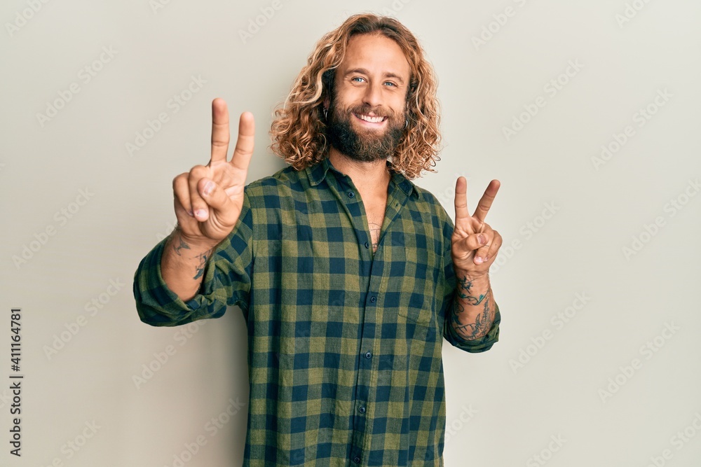 Handsome man with beard and long hair wearing casual clothes smiling looking to the camera showing fingers doing victory sign. number two. Handsome man with beard and long hair wearing casual clothes smiling looking to the camera showing fingers doing victory sign. number two.