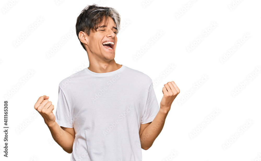 Young hispanic man wearing casual white tshirt very happy and excited doing winner gesture with arms raised, smiling and screaming for success. celebration concept. Young hispanic man wearing casual white tshirt very happy and excited doing winner gesture with arms raised, smiling and screaming for success. celebration concept.