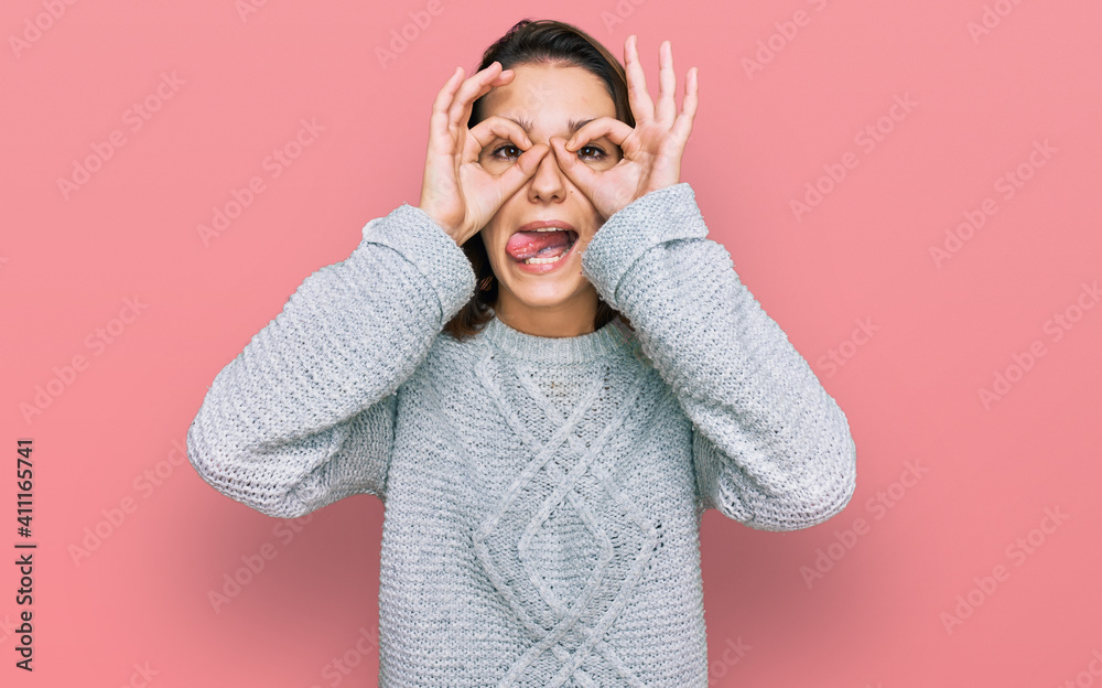 Young caucasian girl wearing casual clothes doing ok gesture like binoculars sticking tongue out, eyes looking through fingers. crazy expression. Young caucasian girl wearing casual clothes doing ok gesture like binoculars sticking tongue out, eyes looking through fingers. crazy expression.
