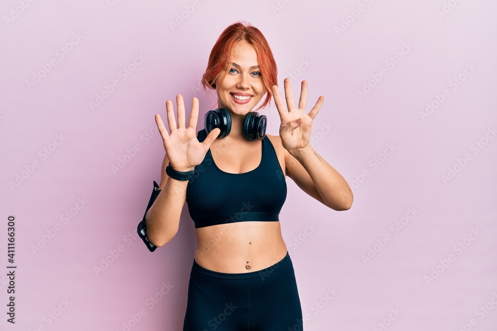 Young beautiful redhead woman wearing gym clothes and using headphones showing and pointing up with fingers number nine while smiling confident and happy. Young beautiful redhead woman wearing gym clothes and using headphones showing and pointing up with fingers number nine while smiling confident and happy.