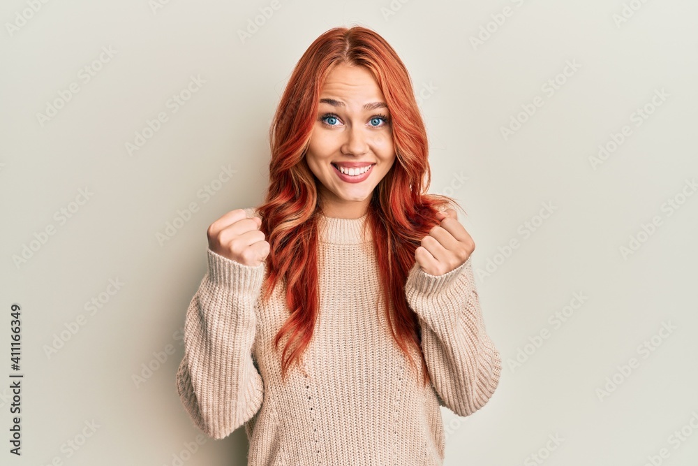Young beautiful redhead woman wearing casual winter sweater celebrating surprised and amazed for success with arms raised and open eyes. winner concept.