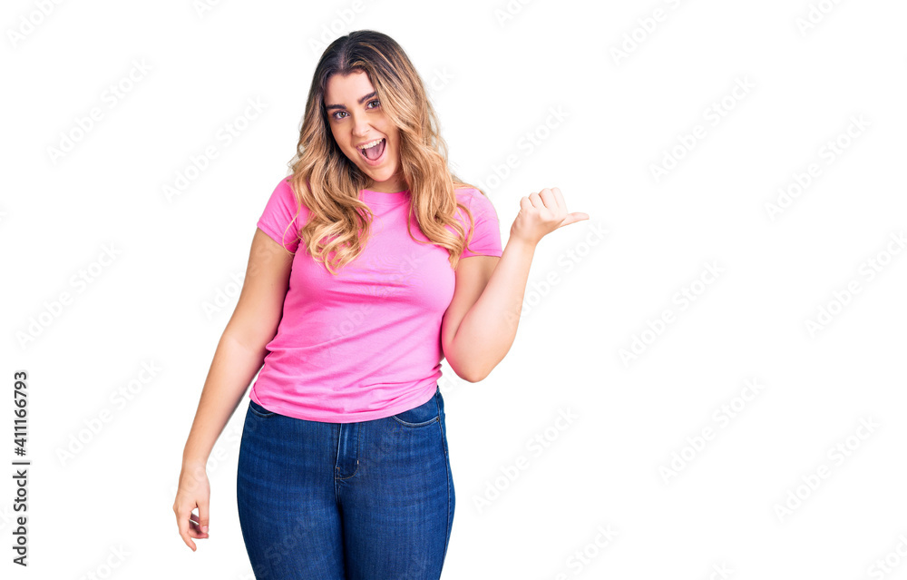 Young caucasian woman wearing sportswear smiling with happy face looking and pointing to the side with thumb up. Young caucasian woman wearing sportswear smiling with happy face looking and pointing to the side with thumb up.