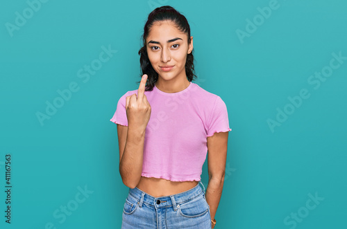 Hispanic teenager girl with dental braces wearing casual clothes showing middle finger, impolite and rude fuck off expression