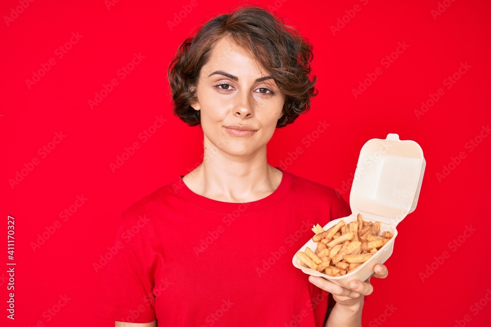 Young hispanic woman holding potato chip thinking attitude and sober expression looking self confident