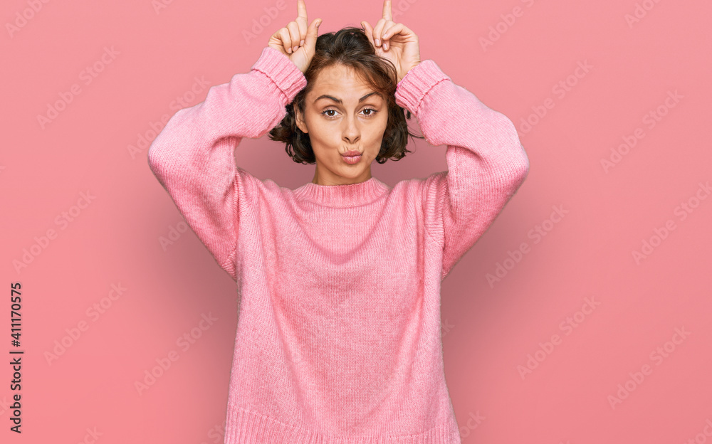 Young hispanic woman wearing casual clothes doing funny gesture with finger over head as bull horns Young hispanic woman wearing casual clothes doing funny gesture with finger over head as bull horns