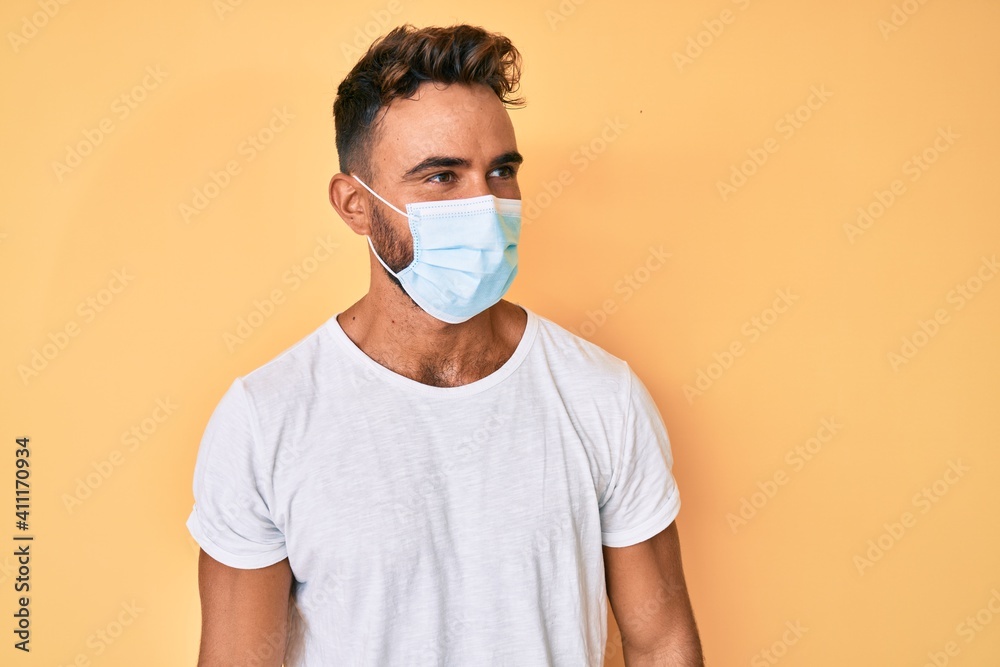 Young hispanic man wearing medical mask looking to side, relax profile pose with natural face and confident smile. Young hispanic man wearing medical mask looking to side, relax profile pose with natural face and confident smile.