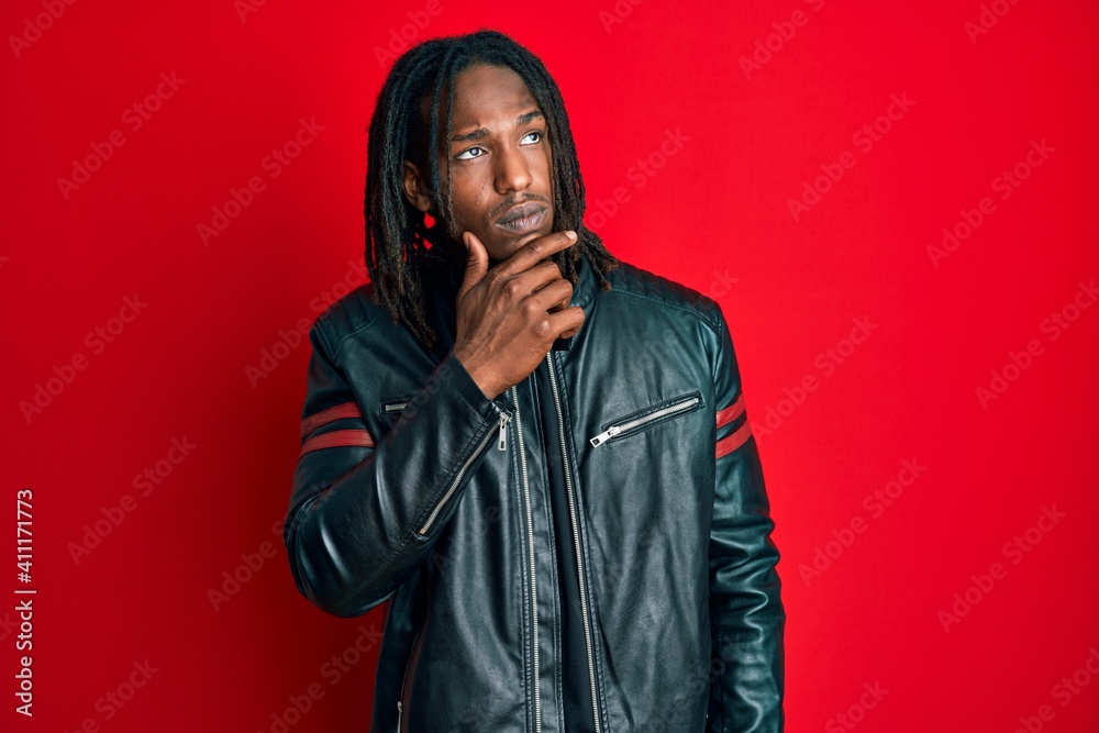 African american man with braids wearing black leather jacket thinking concentrated about doubt with finger on chin and looking up wondering