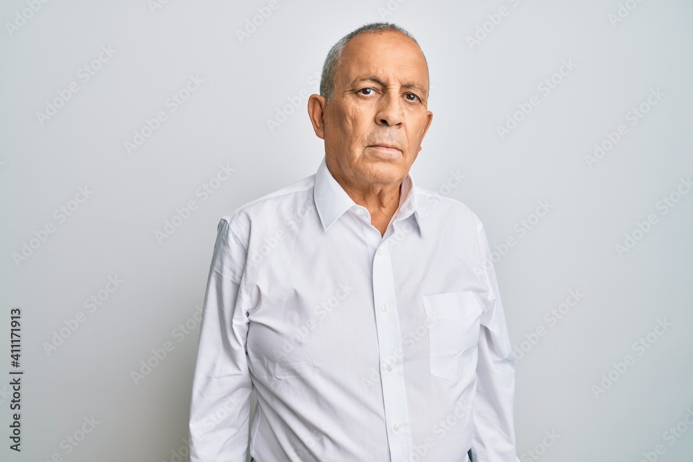 Handsome senior man wearing casual white shirt relaxed with serious expression on face. simple and natural looking at the camera. Handsome senior man wearing casual white shirt relaxed with serious expression on face. simple and natural looking at the camera.