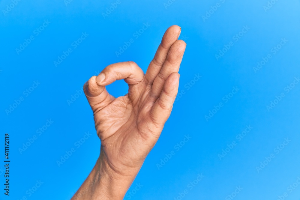 Hand of senior hispanic man over blue isolated background gesturing approval expression doing okay symbol with fingers Hand of senior hispanic man over blue isolated background gesturing approval expression doing okay symbol with fingers