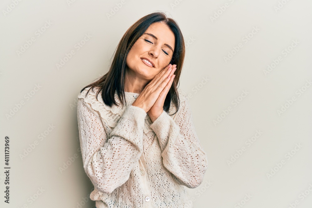 Middle age brunette woman wearing casual clothes sleeping tired dreaming and posing with hands together while smiling with closed eyes. Middle age brunette woman wearing casual clothes sleeping tired dreaming and posing with hands together while smiling with closed eyes.