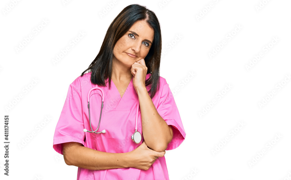 Middle age brunette woman wearing doctor uniform and stethoscope serious face thinking about question with hand on chin, thoughtful about confusing idea Middle age brunette woman wearing doctor uniform and stethoscope serious face thinking about question with hand on chin, thoughtful about confusing idea