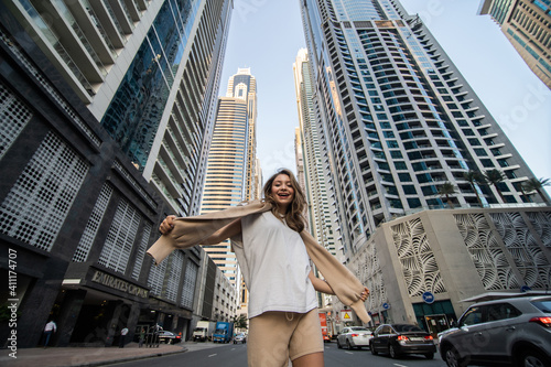 Young casual woman walk with raised hands enjoy the view on downtown skycrapers.