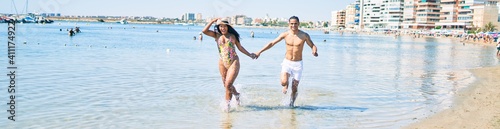 Young latin couple wearing swimwear running at the beach.