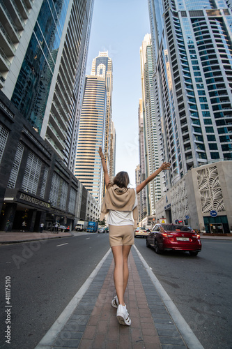Rear view of young woman walking near skycrapers on downtown of modern city.
