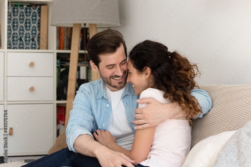 Happy young husband and wife hug on sofa spend time in warm embraces of one another share lovers secrets confessions. Excited newlyweds buying house first time cuddle on couch enjoy new family home Happy young husband and wife hug on sofa spend time in warm embraces of one another share lovers secrets confessions. Excited newlyweds buying house first time cuddle on couch enjoy new family home