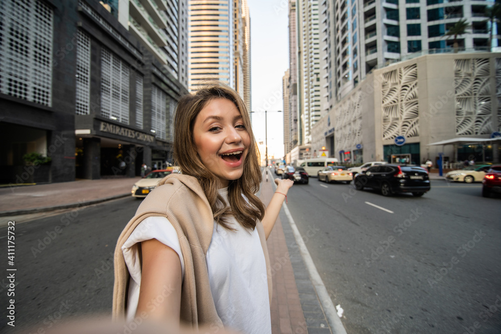 Young woman take selfie photo on the phone with modern skycrapers on background. Low angle