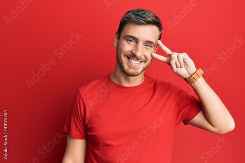 Handsome caucasian man wearing casual red tshirt doing peace symbol with fingers over face  smiling cheerful showing victory