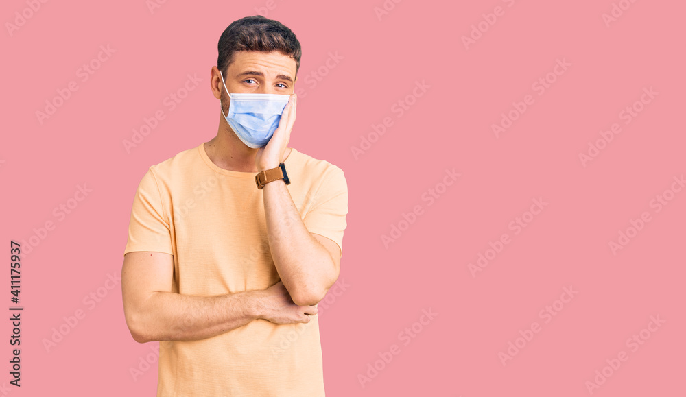 Handsome young man with bear wearing medical mask for coronavirus thinking looking tired and bored with depression problems with crossed arms. Handsome young man with bear wearing medical mask for coronavirus thinking looking tired and bored with depression problems with crossed arms.