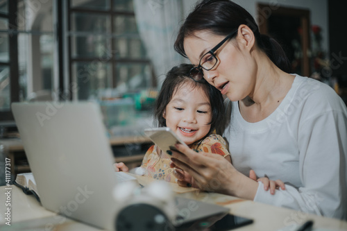 Asian woman teaching her duagther with laptop and smartphone study online concept. photo