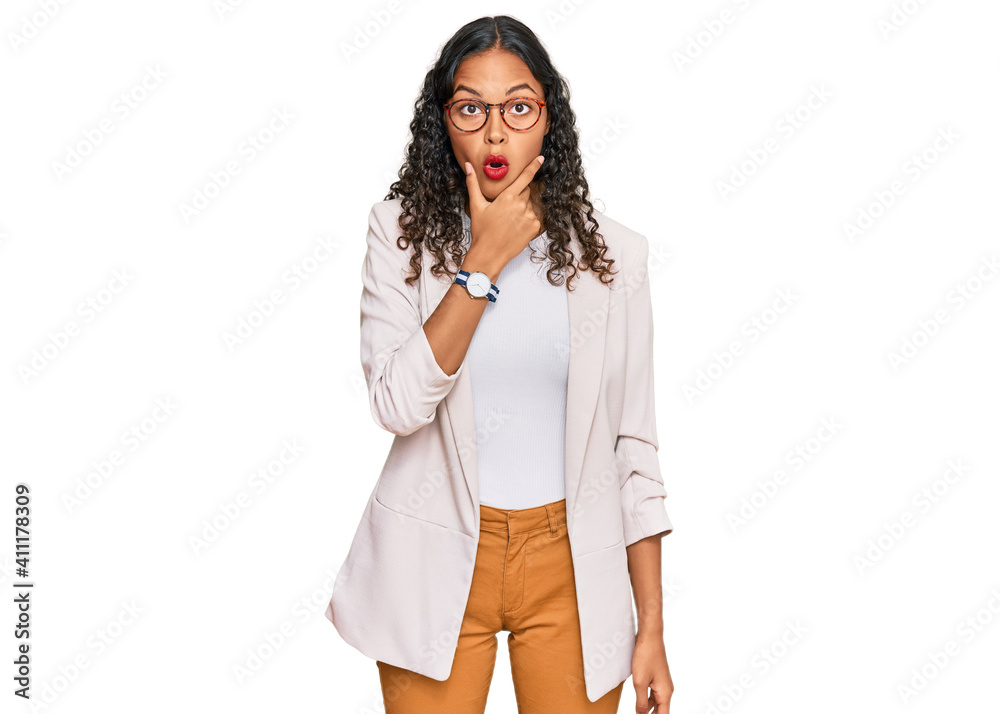 Young african american girl wearing business clothes looking fascinated with disbelief, surprise and amazed expression with hands on chin Young african american girl wearing business clothes looking fascinated with disbelief, surprise and amazed expression with hands on chin