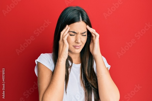 Young brunette woman wearing casual white tshirt over red background with hand on head for pain in head because stress. suffering migraine.