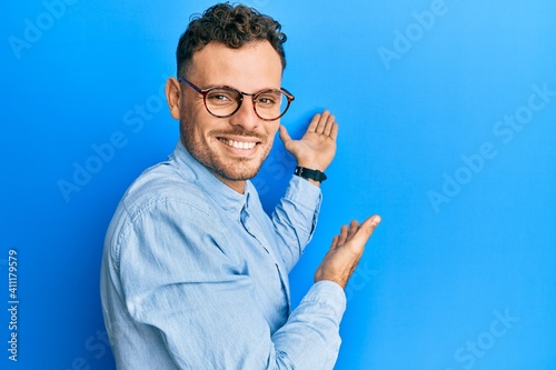 Young hispanic man wearing casual clothes and glasses inviting to enter smiling natural with open hand