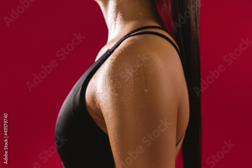 Cropped photo. Girl's body, sweating after physical exertion, on a red background. Dark photo.