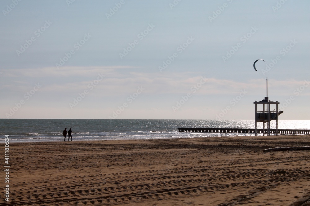 Jesolo, Veneto, Italy: view on the beach during winter with a couple walking and a kitesurf