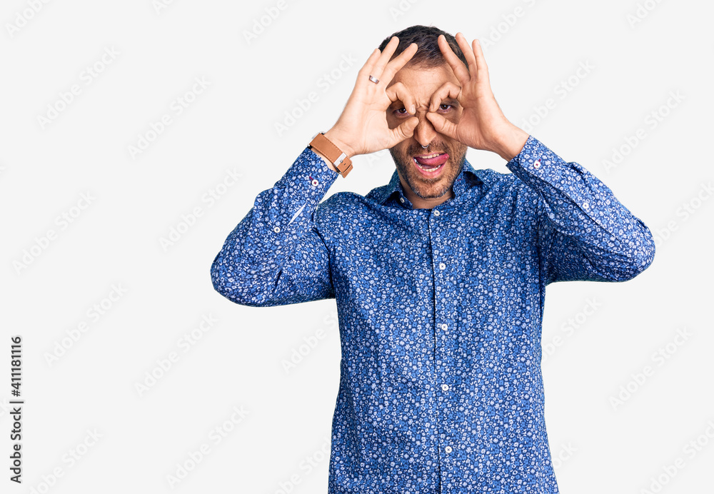 Young handsome man wearing casual clothes doing ok gesture like binoculars sticking tongue out, eyes looking through fingers. crazy expression. Young handsome man wearing casual clothes doing ok gesture like binoculars sticking tongue out, eyes looking through fingers. crazy expression.