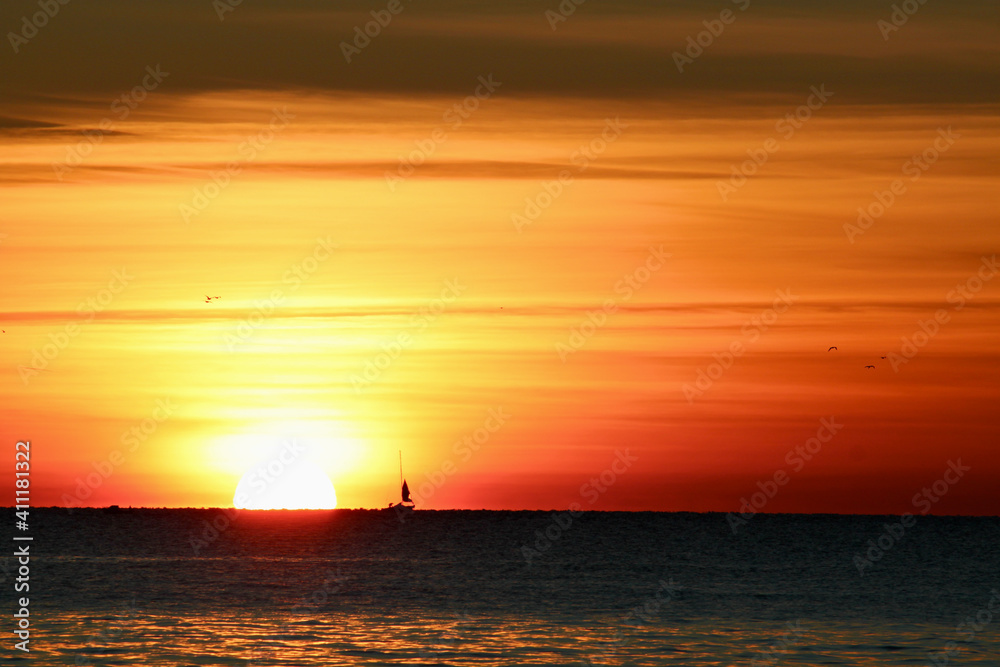Große Sonne bei Sonnenuntergang mit Segelschiff am Horizont links