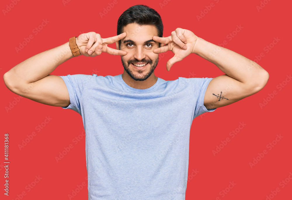 Young hispanic man wearing casual clothes doing peace symbol with fingers over face, smiling cheerful showing victory Young hispanic man wearing casual clothes doing peace symbol with fingers over face, smiling cheerful showing victory