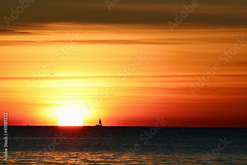 Große Sonne bei Sonnenuntergang mit Segelschiff am Horizont links