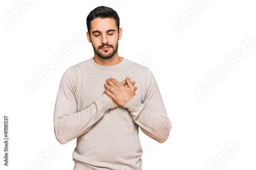 Young hispanic man wearing casual clothes smiling with hands on chest with closed eyes and grateful gesture on face. health concept.