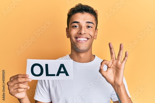 Young handsome african american man holding ola as portuguese greeting doing ok sign with fingers, smiling friendly gesturing excellent symbol © Krakenimages.com