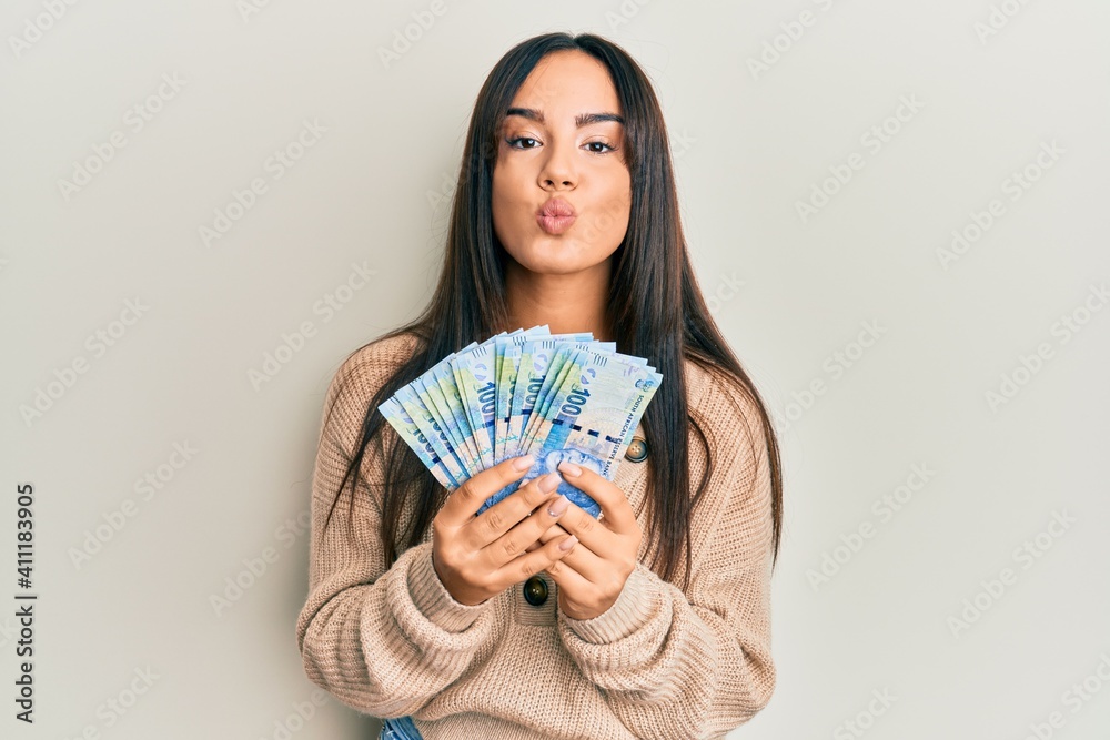 Young beautiful hispanic girl holding south african 100 rand banknotes looking at the camera blowing a kiss being lovely and sexy. love expression. Young beautiful hispanic girl holding south african 100 rand banknotes looking at the camera blowing a kiss being lovely and sexy. love expression.