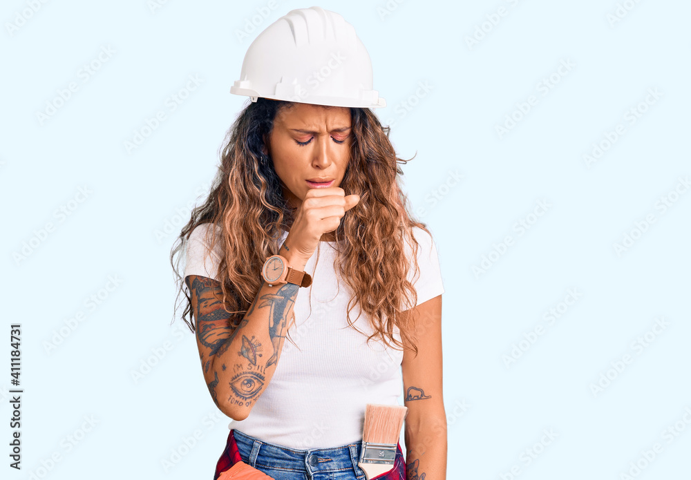 Young hispanic woman with tattoo wearing hardhat and builder clothes feeling unwell and coughing as symptom for cold or bronchitis. health care concept. Young hispanic woman with tattoo wearing hardhat and builder clothes feeling unwell and coughing as symptom for cold or bronchitis. health care concept.