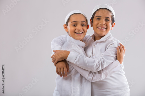 Young Muslim boys with caps side hugging each other 