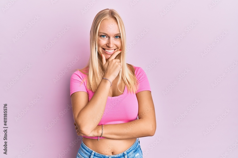 Young blonde girl wearing casual clothes looking confident at the camera smiling with crossed arms and hand raised on chin. thinking positive. Young blonde girl wearing casual clothes looking confident at the camera smiling with crossed arms and hand raised on chin. thinking positive.