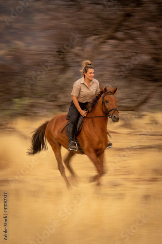 Slow pan of blonde riding near trees © Nick Dale