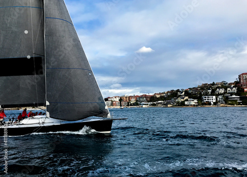 Commanding yacht racing in Sydney Harbor. Medium shot of the boat with cloudy dramatic sky and Eastern Suburbs behind