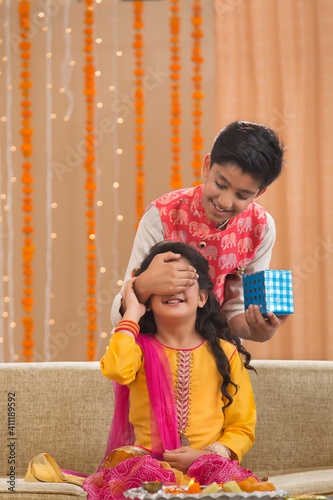 Фотография young brother surprising his sister with a  present
