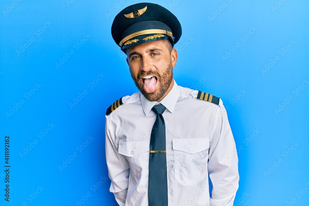Handsome man with beard wearing airplane pilot uniform sticking tongue out happy with funny expression. emotion concept. Handsome man with beard wearing airplane pilot uniform sticking tongue out happy with funny expression. emotion concept.