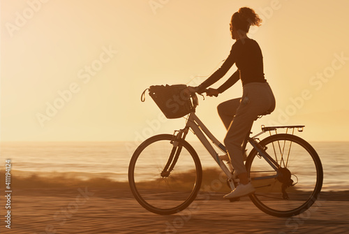 Woman traveler with her bicycle rides on sea coastline and looking on beautifull sunset sky in sunny summer day on beach