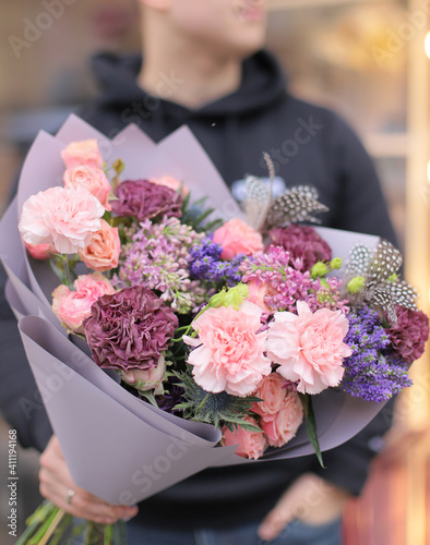 Strong man holding a delicate bouquet of beautiful flowers in his hands. Delicate flower bouquet. Wrapped flowers bouquet. Fresh beautiful flower. Man holding a big beautiful flowers bouquet.